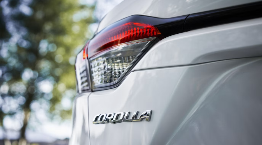 Close-up of the polished chrome emblem and taillight on a white 2026 Toyota Corolla, representing reliable commuter cars in Lake County for Waukegan and Gurnee, IL drivers.