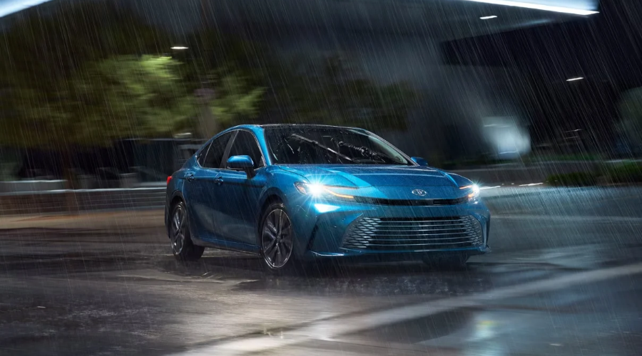 Front view of a blue 2026 Toyota Camry Hybrid AWD driving safely through heavy rain on a wet slick road at night, demonstrating TSS 3.0 wet weather traction for Waukegan IL drivers at Classic Toyota